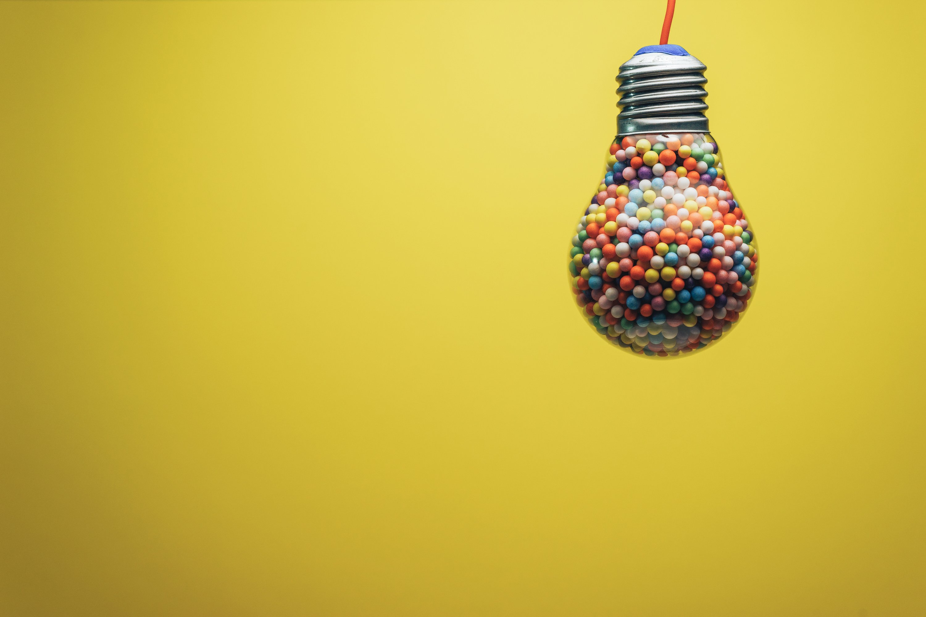 Creative lightbulb filled with multi colored ball on a yellow background behind. Best idea concept.